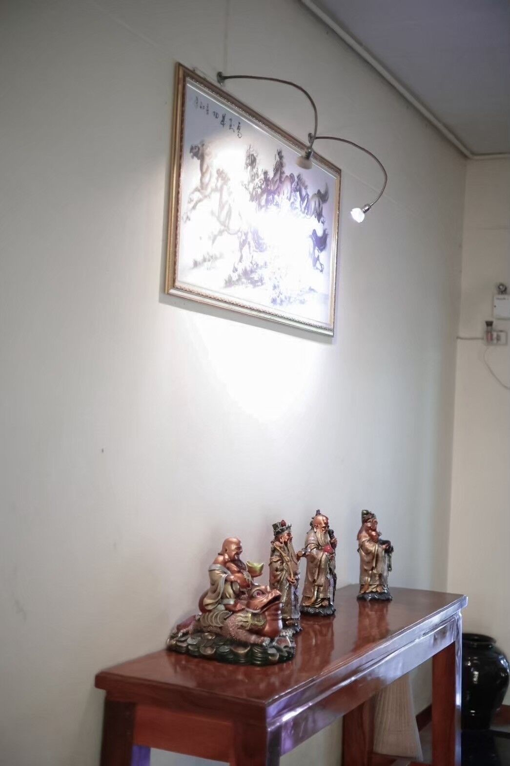 Et indrammet kunstværk på væggen, et træbord med figurer, og en lampe.
