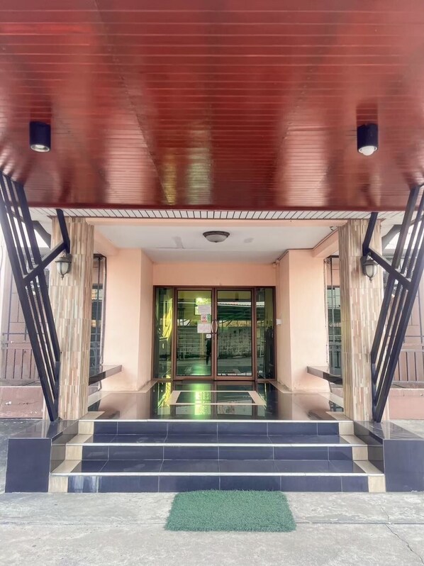 L’entrée d’un hôtel au design moderne, avec une porte en verre, un escalier en métal et un tapis de gazon synthétique vert au bas.