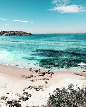 Une plage à l’eau turquoise et limpide, un rivage rocheux et une ville qui se devine au loin.
