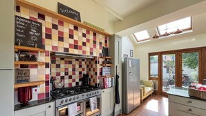 A kitchen with a gas stove, oven, and a refrigerator. There is a chalkboard with a weather board and a welcome sign.