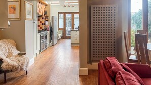A modern kitchen with a stove, refrigerator, and wooden flooring. There is a dining area with a red sofa and a table.