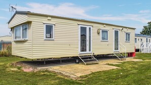 A single-story mobile home with a number '50' on the side, a front door, and a small porch area. - Praise Machine Caravan Experience (St Osyth)