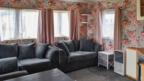 A room with a sofa, a table, and a TV. - Praise Machine Caravan Experience (St Osyth)