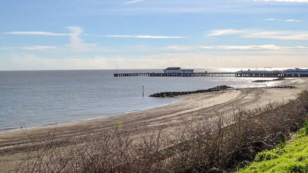 A coastal scene with a pier extending into the water, a sandy beach, and sparse vegetation. - Praise Machine Caravan Experience (St Osyth)