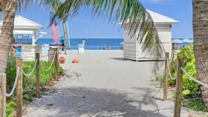 A beach pathway leading to a beach area with a lifeguard tower, beach umbrellas, and a clear view of the ocean. - Gorgeous Ocean View 3BD Condo in Beachfront Resort 907 (Miami Beach)