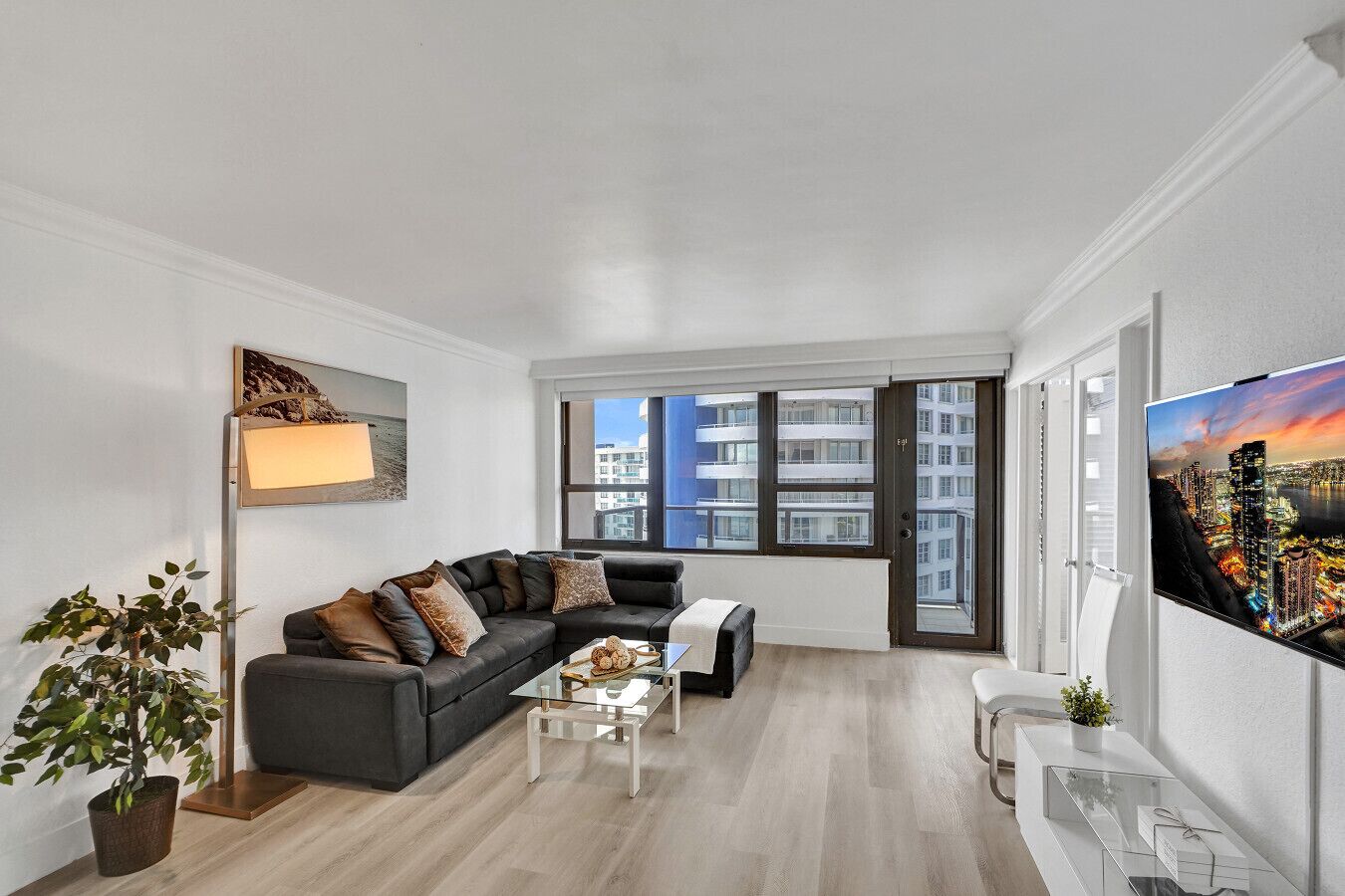 A modern living room with a sectional sofa, a glass coffee table, and a large TV on the wall.