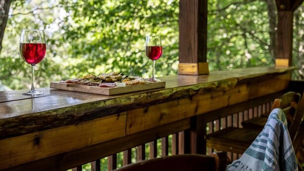 A wooden deck with a table set for two, featuring a glass of red wine and a plate of food. - Secluded Mountain Top with Game Room and Fire Pit Near Boone (Boone)