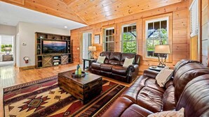 A spacious living room with a wooden ceiling, leather sofas, a television, and a fireplace. - Secluded Mountain Top with Game Room and Fire Pit Near Boone (Boone)