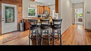 A kitchen with wooden cabinets, a central island with bar stools, and a view of the outdoors through a window. - Secluded Mountain Top with Game Room and Fire Pit Near Boone (Boone)