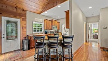 A kitchen with wooden cabinets, a central island with bar stools, and a view of the outdoors through a window.