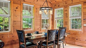 A wooden cabin dining room with a table set for four, large windows with blinds, and a hanging light fixture. - Secluded Mountain Top with Game Room and Fire Pit Near Boone (Boone)