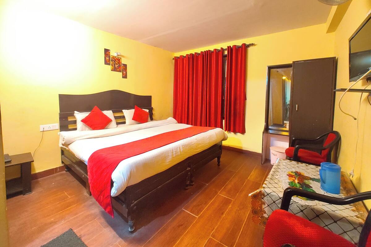 A bedroom with a bed, a chair, a desk, a mirror, and a red curtain.