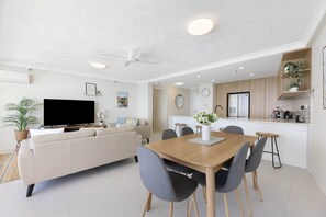 Un salon moderne comprenant un canapé, un téléviseur et un coin repas avec des chaises et une table.