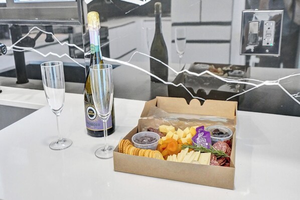 Une table avec une bouteille de champagne, deux verres et une boîte de diverses collations.