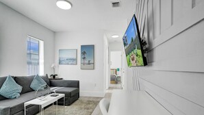 A modern living room with a grey sofa, white coffee table, and a flat-screen TV mounted on the wall. - Palm Breeze Retreat . Close to Beach & Downtown (Hollywood)