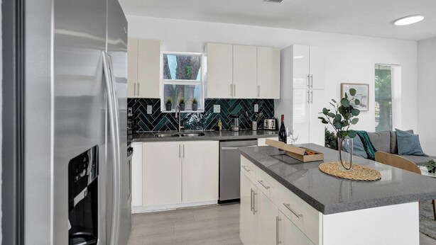 A modern kitchen with white cabinets, a black backsplash, and stainless steel appliances. - Palm Breeze Retreat . Close to Beach & Downtown (Hollywood)