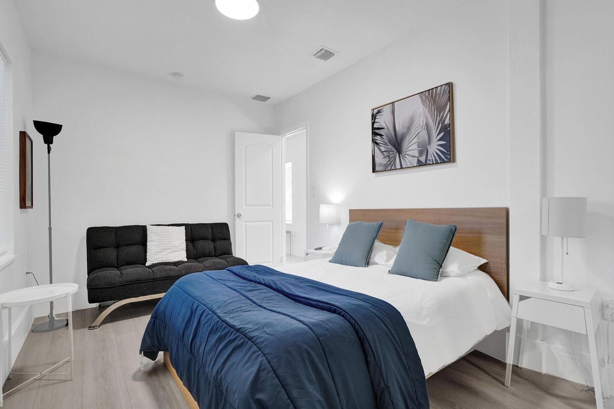 Una habitación de hotel moderna con una cama grande, un sofá oscuro, una mesita y una lámpara.