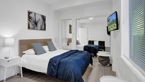 A modern hotel room with a large bed, a TV, a mirror, and a window with blinds. - Palm Breeze Retreat . Close to Beach & Downtown (Hollywood)