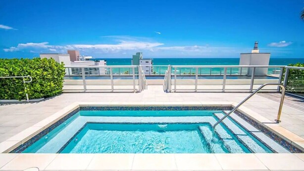 A rectangular swimming pool with clear blue water, surrounded by a tiled deck and metal railings. - New Luxury Beachfront Condo with Rooftop Pool (Hollywood)