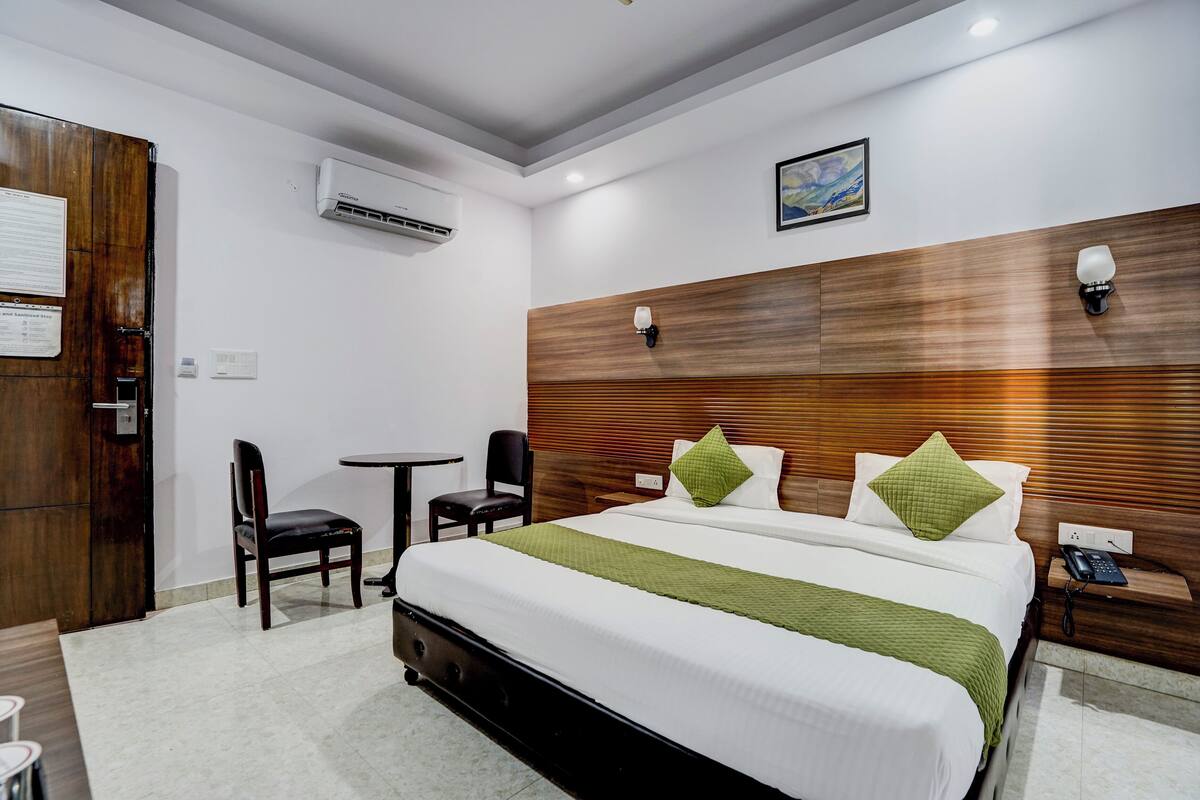 A hotel room with a large bed, a wooden headboard, a desk with a chair, and a small table.