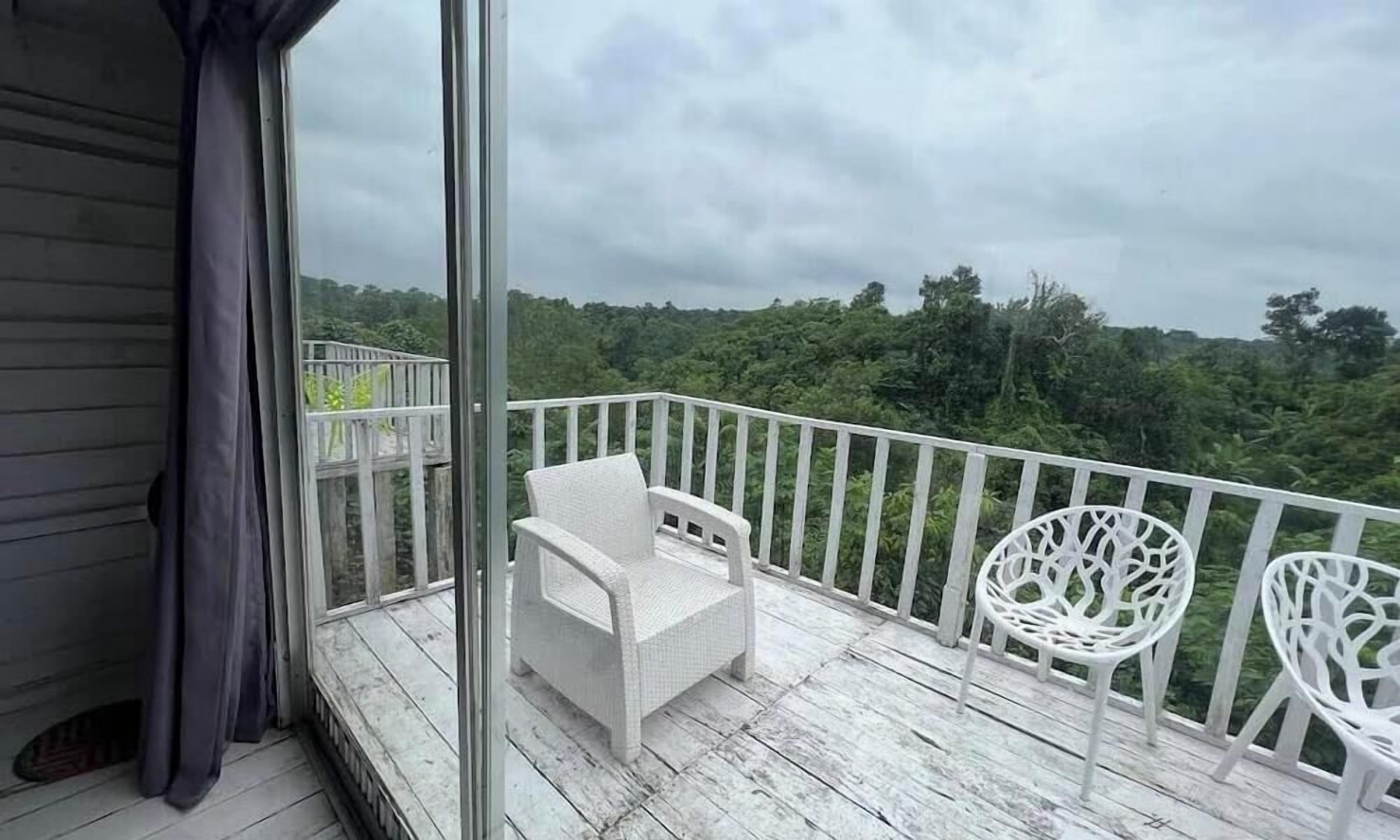 Varanda com mobiliário de vime branco e vista para uma área arborizada.
