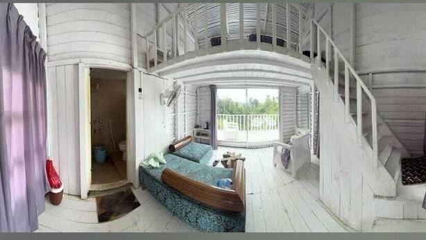 A room with a wooden staircase, a bed with a blue bedspread, and a view of the outdoors.