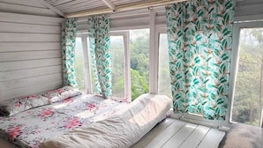 A bedroom with a bed, floral curtains, and a view of greenery outside.