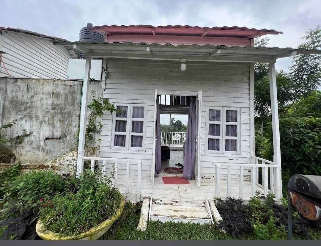 Uma casa pequena, térrea, com varanda, telhado vermelho e porta visível para o interior.
