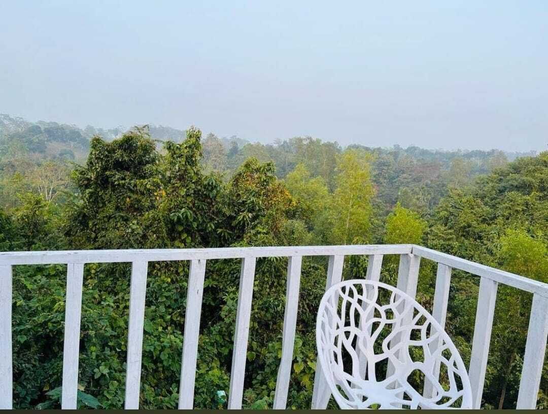 Barandilla blanca con una silla blanca, con vistas a un paisaje boscoso y denso.