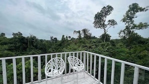 A wooden deck with two white chairs and a railing, overlooking a dense forest.