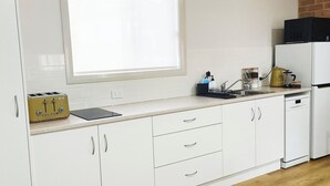 Una cucina con mobili bianchi, una finestra con persiane, un tostapane, un bollitore e un forno a microonde.