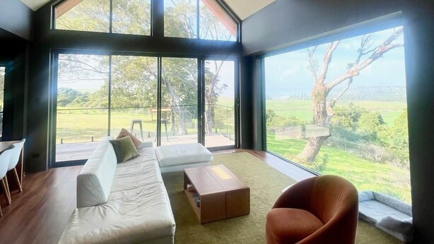Uma sala de estar moderna com uma janela grande, um sofá branco, uma poltrona vermelha e uma mesa pequena.