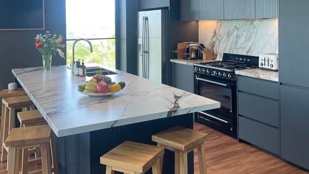 Una cocina moderna con una isla grande, taburetes de madera, horno empotrado y refrigerador de acero inoxidable.