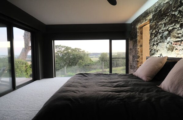 Un dormitorio con una cama grande, una pared de piedra y vistas al exterior.