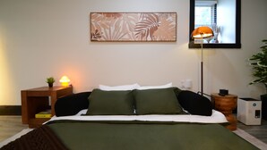 A neatly made bed with a green bedspread, a bedside lamp, a small plant on the nightstand, and a large abstract painting on the wall. - Bluff Street Escape • Modern 1BR Near Downtown (Dubuque)