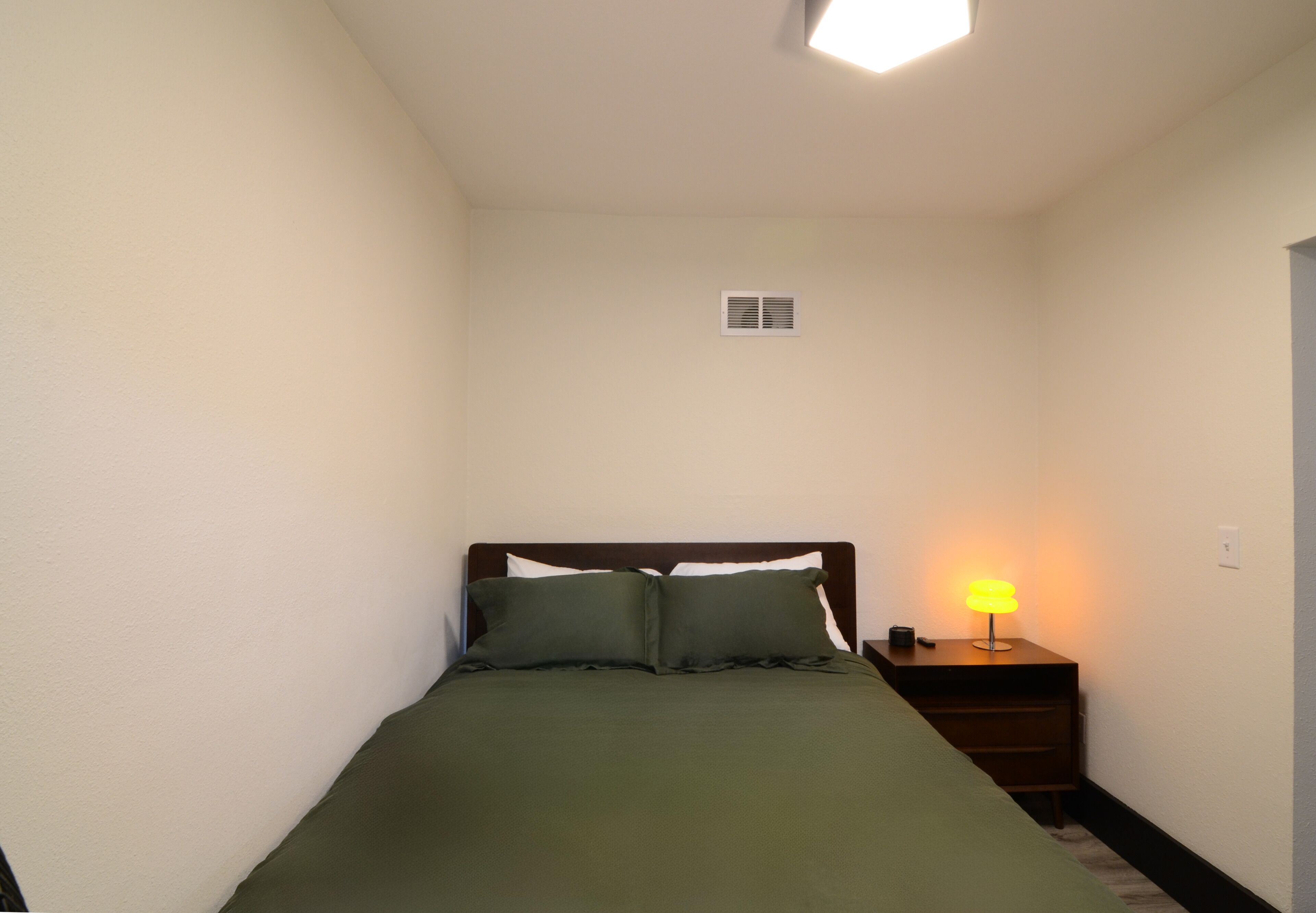 A small, neatly made room with a single bed, a bedside lamp, and a nightstand.
