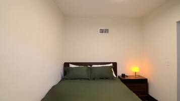 A small, neatly made room with a single bed, a bedside lamp, and a nightstand.