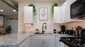 A modern kitchen with white cabinets, a granite countertop, a black faucet, and a stainless steel stove. - Bluff Street Escape • Modern 1BR Near Downtown (Dubuque)