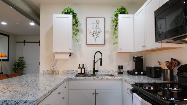 A modern kitchen with white cabinets, a granite countertop, a black faucet, and a stainless steel stove. - Bluff Street Escape • Modern 1BR Near Downtown (Dubuque)