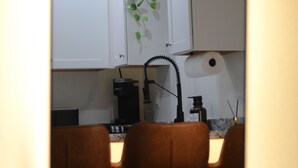 A mirror reflecting a kitchen area with white cabinets, a countertop, and two brown bar stools. - Bluff Street Escape • Modern 1BR Near Downtown (Dubuque)