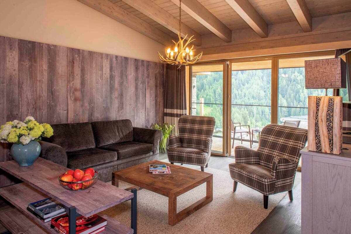 Una sala de estar acogedora con techo de madera, un sofá, dos sillones a cuadros, una mesa de centro y una estantería.