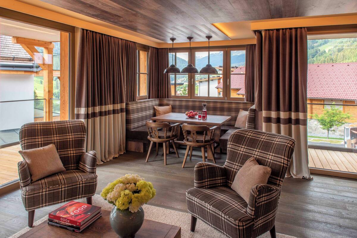 Un comedor acogedor con mobiliario escocés, una mesa de madera y vistas a un pueblo de montaña a través de amplias ventanas.