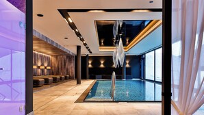 Un área de piscina interior moderna con vista despejada, asientos a lo largo de las paredes e iluminación empotrada en el techo.