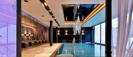 Uma área moderna de piscina interna com vista desobstruída, assentos ao longo das paredes e teto com iluminação embutida.