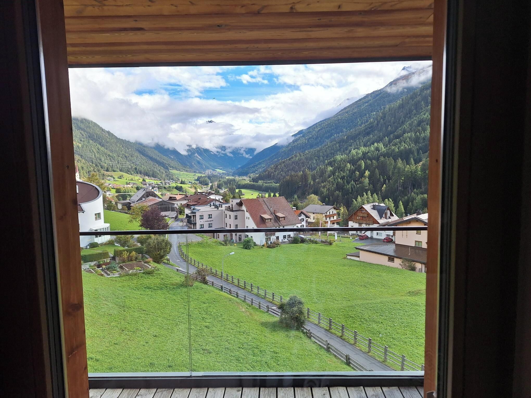 Une vue depuis une fenêtre donnant sur une vallée, avec des bâtiments, une route et des montagnes.