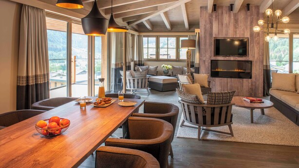 Amplia sala de estar con una mesa de comedor de madera, asientos cómodos, una chimenea y un televisor montado en la pared.