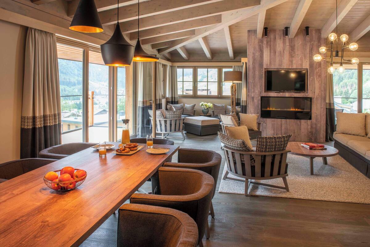 Amplia sala de estar con una mesa de comedor de madera, asientos cómodos, una chimenea y un televisor montado en la pared.