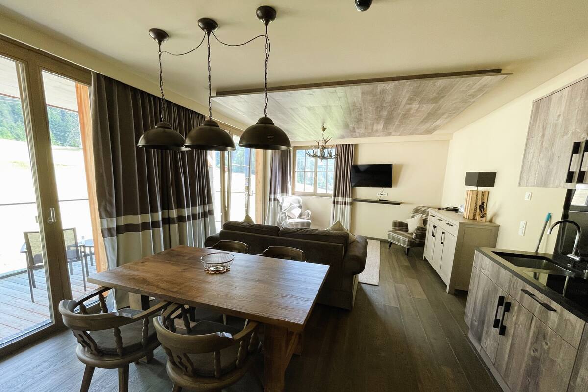 Una cocina moderna con una mesa y sillas de madera, una zona de comedor con sofá y un televisor montado en la pared.