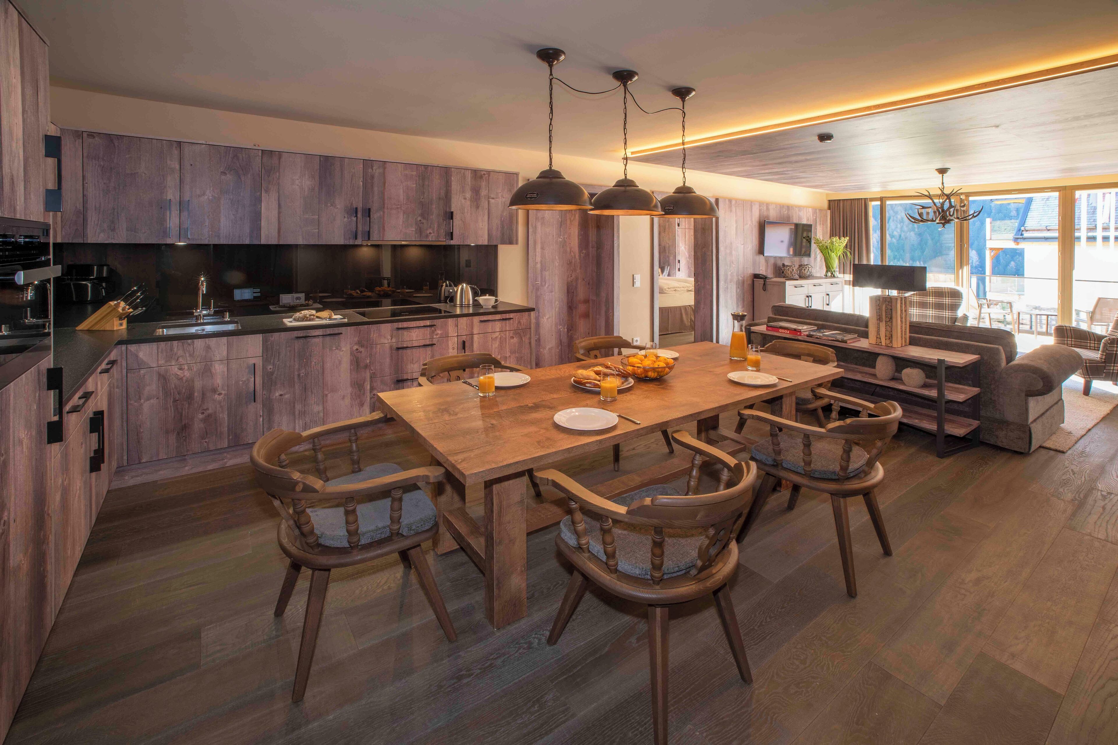 A modern kitchen with wooden cabinets, a dining area with a wooden table and chairs, and a living area with a sofa and a TV.