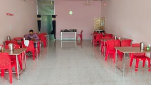 A dining area with red chairs and tables, a person sitting at a table, and a counter with a cash register.